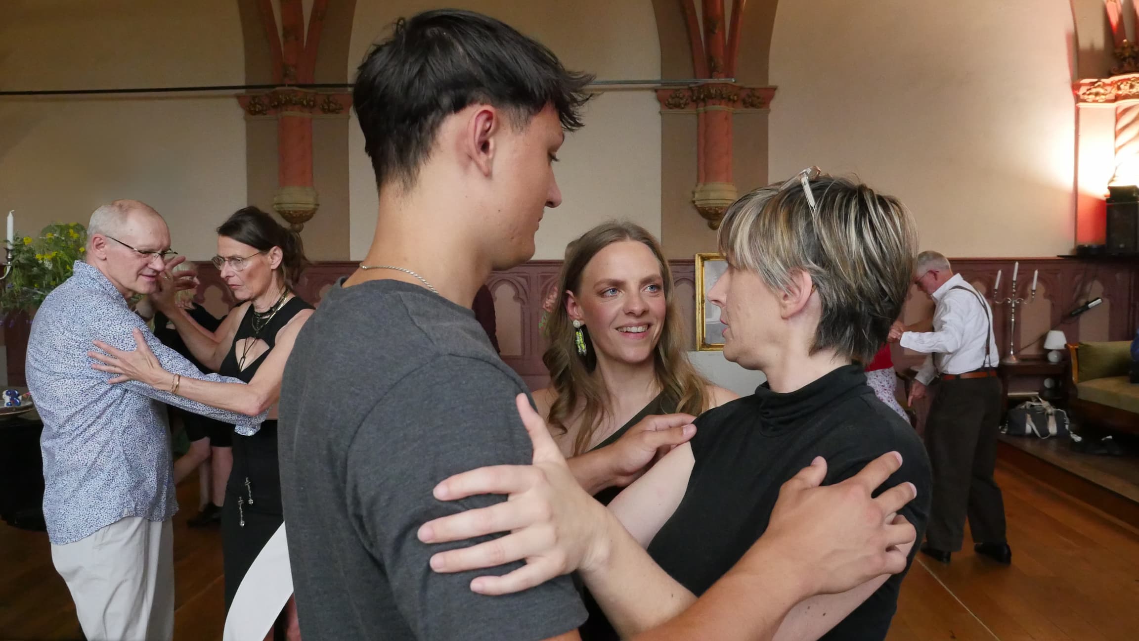 Tänzerin erhält individuelles Feedback von der Lehrerin Juliana, daneben ihr Tanzpartner, im Hintergrund weitere übende Paare
